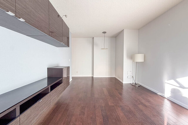 Long open living and dining room with a pendant light at the far end and hardwood floors throughout. - 304-827 West 16th Street, North Vancouver
