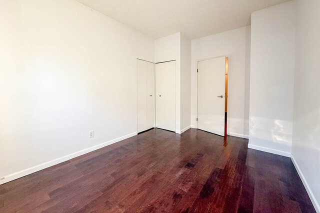 Bedroom with a double closet, white walls and hardwood floors. - 304-827 West 16th Street, North Vancouver