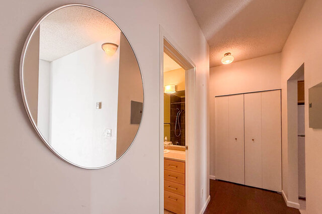Hallway with a round mirror, a double closet and the bathroom door, hardwood floors. - 304-827 West 16th Street, North Vancouver