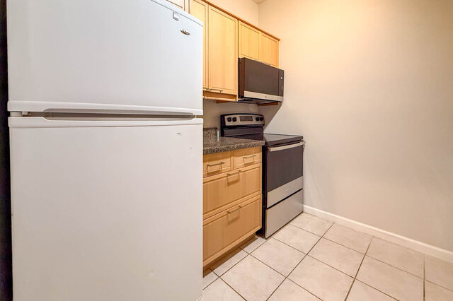 Kitchen with a fridge, a new electric range and microwave, wood cabinets and granite countertops, tile floors.