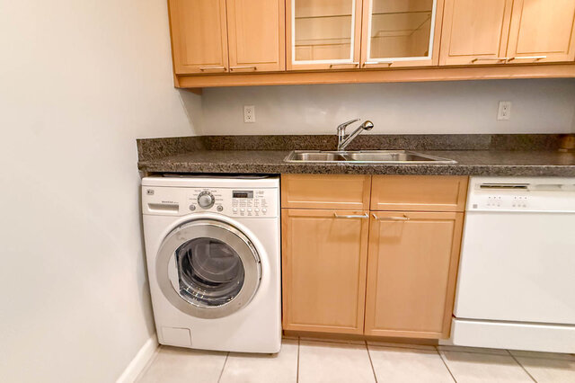 Washer-dryer under the granite counter beside the double sink and dishwasher, wood cabinets above. - 304-827 West 16th Street, North Vancouver