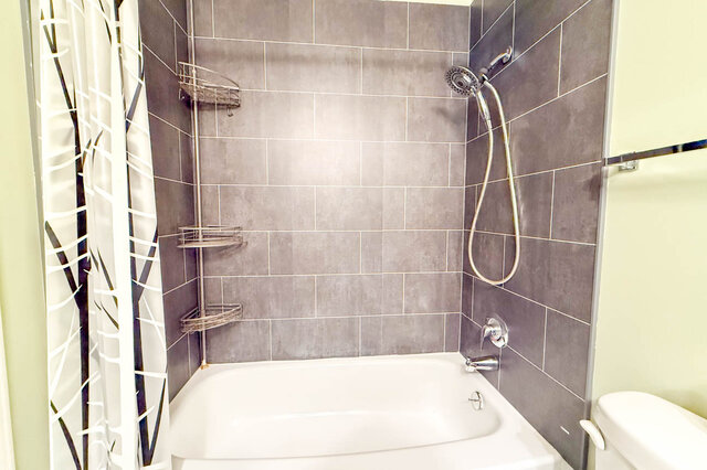 Refinished bathtub with a grey tile surround and a handheld shower. - 304-827 West 16th Street, North Vancouver