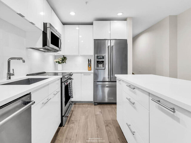 Close view along the kitchen: white gloss cabinets, an undermount sink, a stainless steel range and a French-door fridge besi