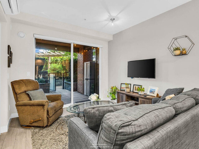 Living room with a sofa, recliner and wall-mounted TV; sliding glass doors open to the covered patio, with a wall air conditi
