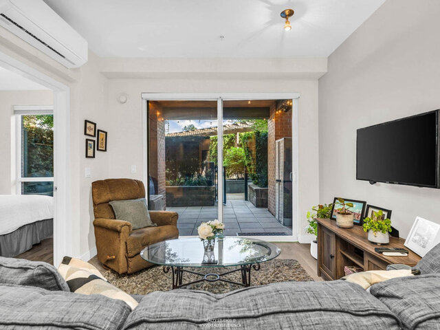 Living room looking out through sliding glass doors to the covered patio and garden; the bedroom doorway on the left and an a