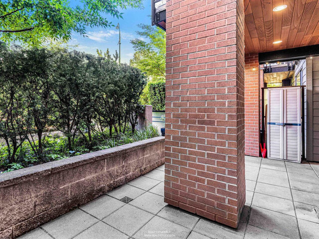 Patio corner with a brick column, a low planter wall with hedges and a covered section with a cedar ceiling and a storage cab