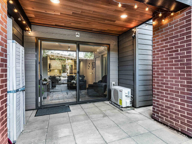 Covered patio under a cedar ceiling with string lights, facing the sliding glass doors into the living room; an air condition