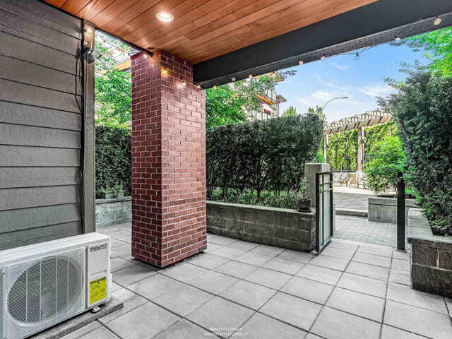 Covered patio with a brick column, stone pavers and string lights; a gate opens toward the garden courtyard and pergola.