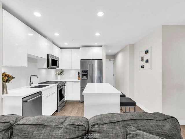 Kitchen seen from the sofa: white gloss cabinets, stainless steel appliances and an island with stools. - 117-723 3rd street West, North Vancouver