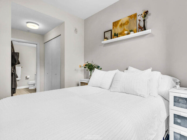 Bedroom with a large bed, a floating shelf and a closet; a walkway leads through to the bathroom. - 117-723 3rd street West, North Vancouver
