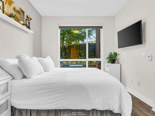 Bedroom with a large window onto trees and the garden, a wall-mounted TV and a large bed. - 117-723 3rd street West, North Vancouver