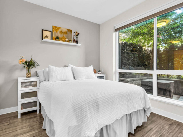 Bedroom with a big window looking onto greenery and the patio, a large bed and two nightstands. - 117-723 3rd street West, North Vancouver