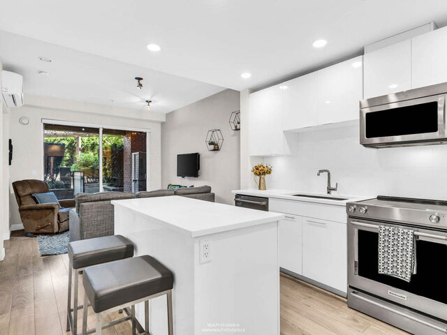 Kitchen island with two stools and white gloss cabinets, open to the living room and the patio doors. - 117-723 3rd street West, North Vancouver