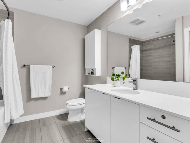 Bathroom with a long white vanity with drawers, a large mirror and the tub with shower. - 117-723 3rd street West, North Vancouver