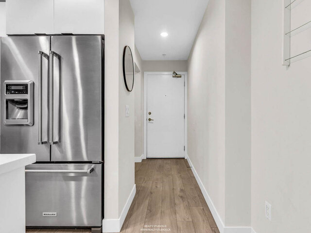 Entry hallway from the kitchen fridge to the front door, with a round mirror and hardwood floors. - 117-723 3rd street West, North Vancouver