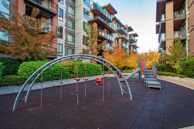Shared playground in the courtyard between the buildings with climbing arches, a slide and autumn trees. - 117-723 3rd street West, North Vancouver