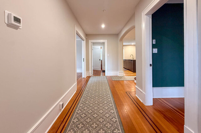 Long main hall with inlaid hardwood floors and an arched doorway through to the kitchen. - North Vancouver