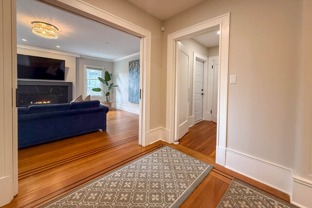 Living room seen from the hall, with a fireplace, a crystal ceiling light and hardwood floors. - North Vancouver