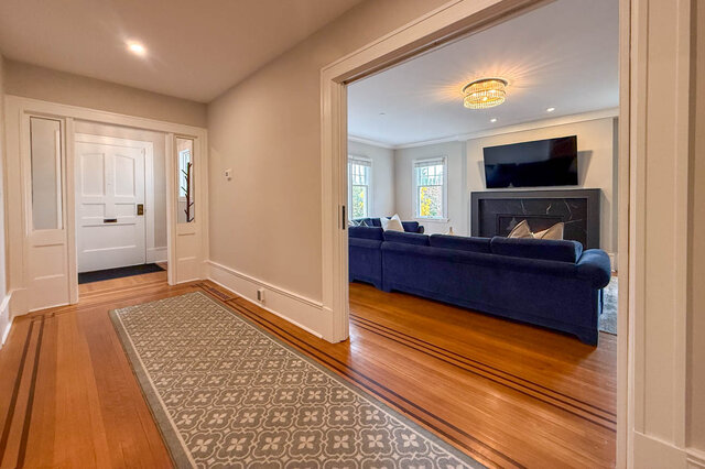Living room through open pocket doors, with the fireplace, windows and the front door behind. - North Vancouver