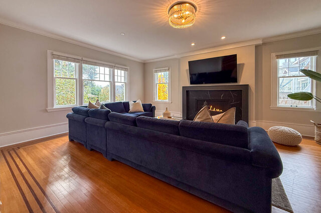 Formal living room with a fireplace in a black stone surround, a crystal ceiling light, a bank of windows and hardwood floors - North Vancouver