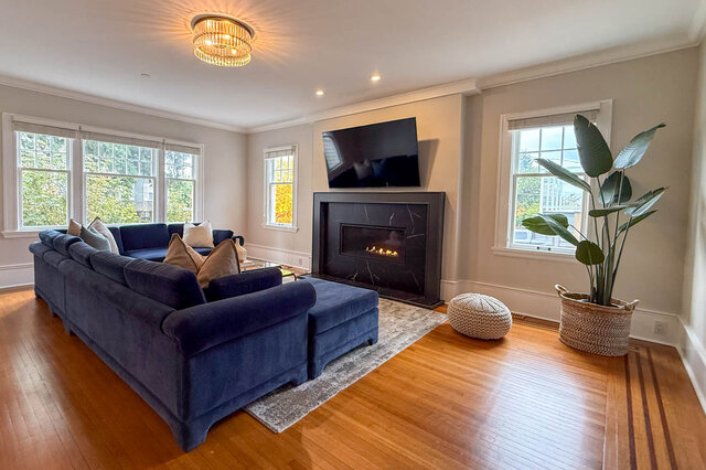 Living room with a fireplace in a black stone surround, crown moulding, large windows and inlaid hardwood floors. - North Vancouver