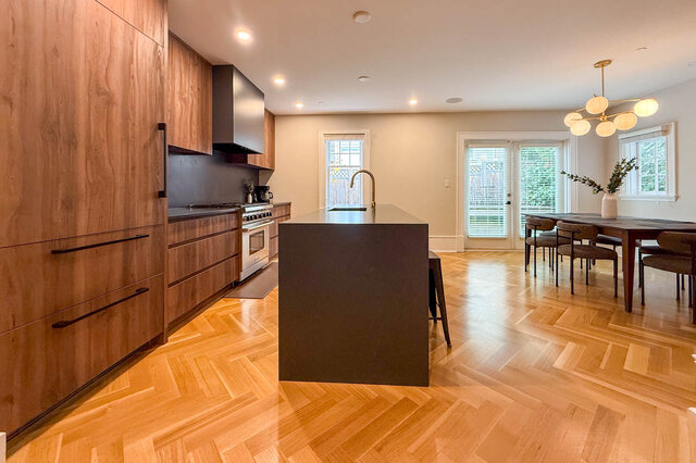 Kitchen with wood-grain cabinets, a professional range, a dark waterfall island with a brass faucet and herringbone floors, o - North Vancouver