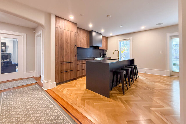 Kitchen with a long waterfall island and bar seating, a panelled fridge and herringbone floors. - North Vancouver