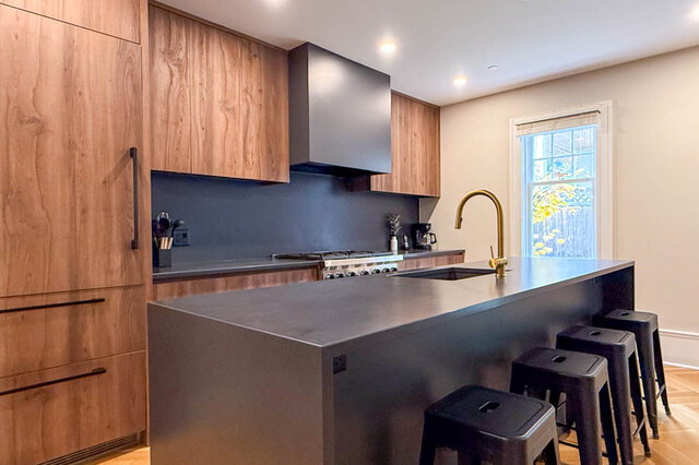 Kitchen with a dark waterfall island, a brass faucet, a professional range and a dark stone backsplash. - North Vancouver