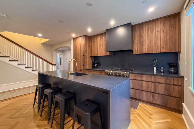 Kitchen with a professional range, wood-grain cabinets, a waterfall island and the staircase beside it. - North Vancouver