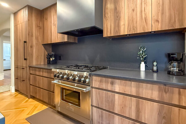 Professional stainless range with a dark backsplash and wood-grain cabinets. - North Vancouver
