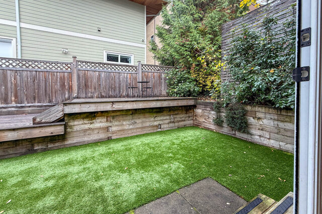 Fenced back yard with artificial turf, a raised wood deck and timber retaining walls. - North Vancouver