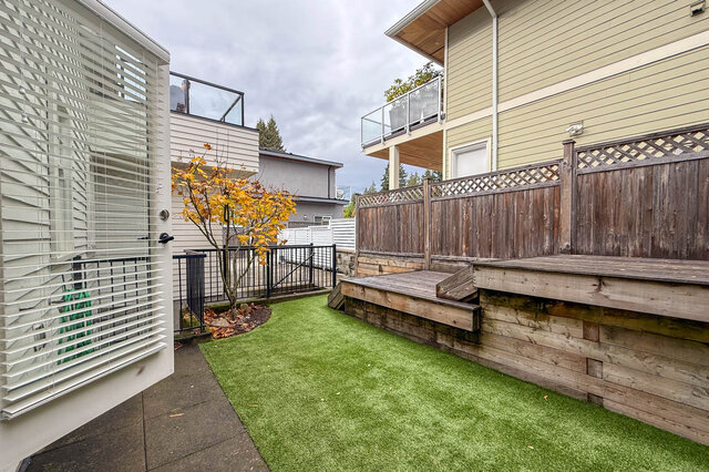 Back yard with artificial turf, wood deck steps, a fence and a maple tree. - North Vancouver