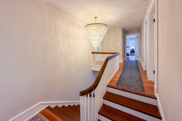 Upper landing with a tiered crystal chandelier, the staircase and the hall to the bedrooms. - North Vancouver