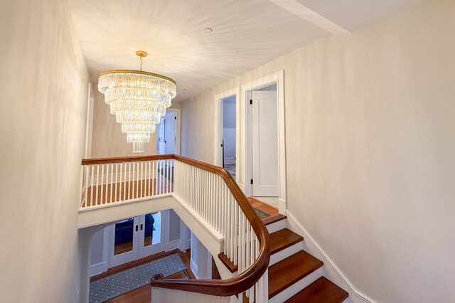 Staircase rising under a tiered crystal chandelier to the upper landing. - North Vancouver