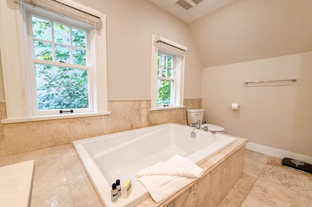 Soaker tub in a stone surround under two windows onto the trees. - North Vancouver