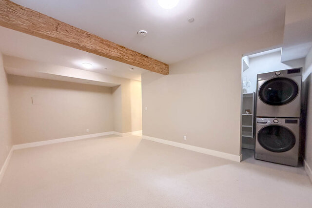 Finished basement flex space with carpet, a wood ceiling beam and laundry with a stacked washer and dryer. - North Vancouver